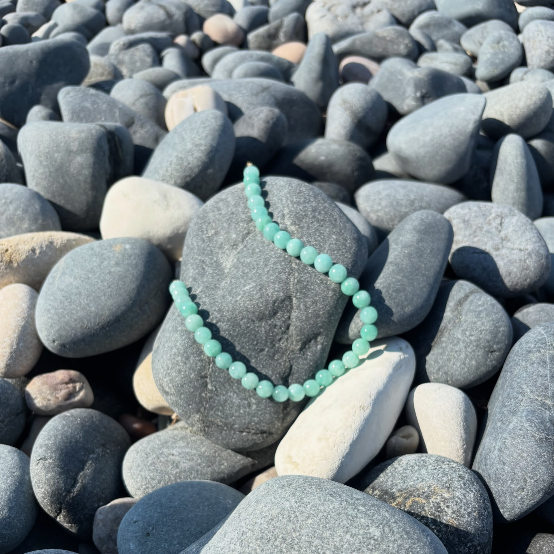 Mint green stone necklace resting on sea pebbles